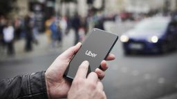 A photo illustration shows a man holding a smartphone with the Uber transport app visible on screen, while taxis queue in the background, on June 4, 2019, in London , England. (Photo by Olly Curtis/Future via Getty Images)